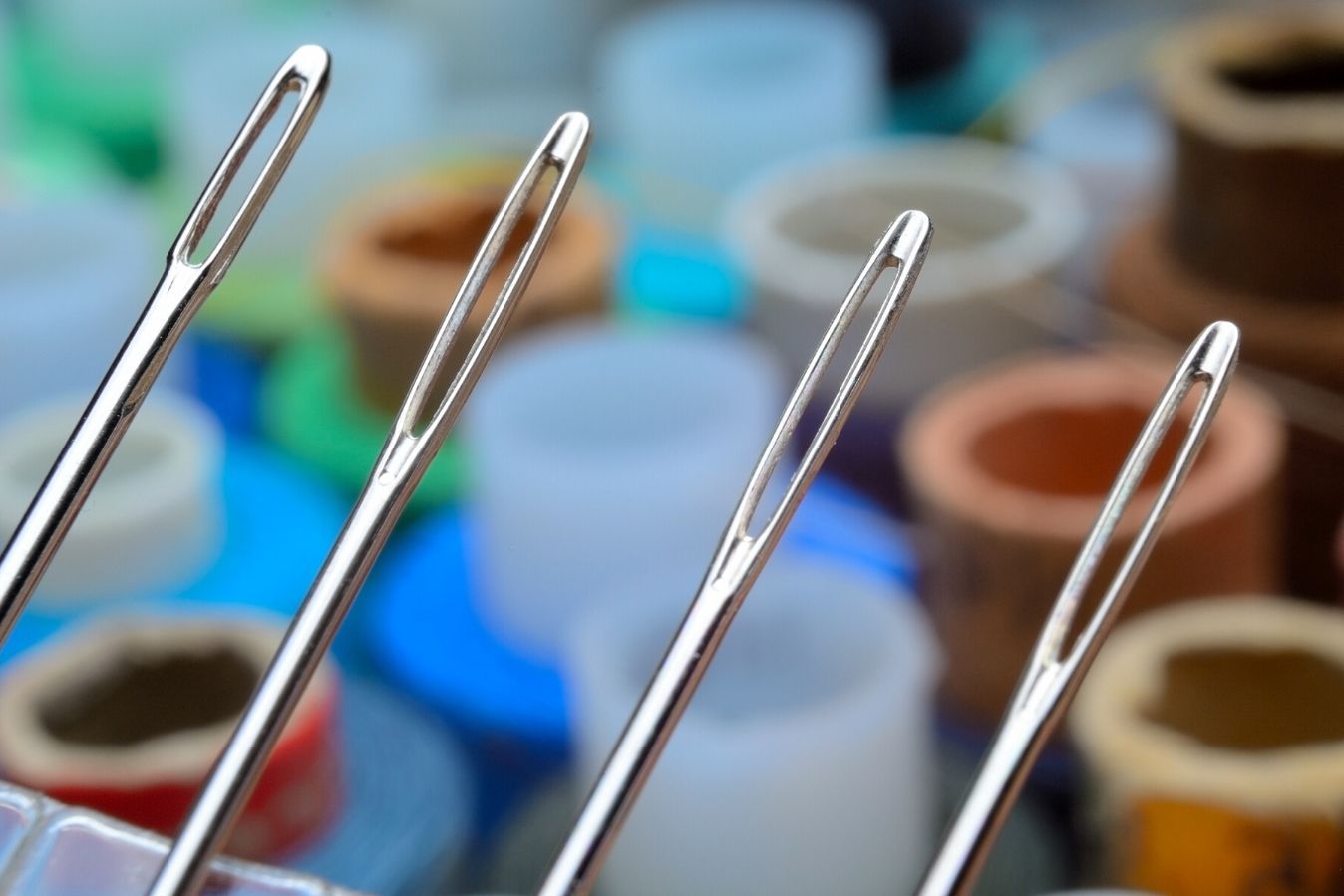 A close-up of three sewing needles with thread in the background.